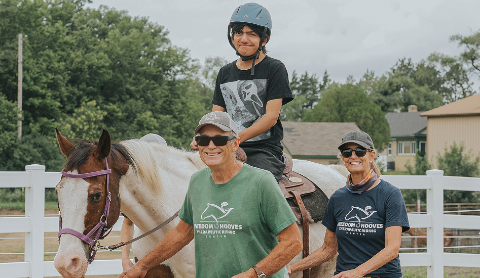 boy in black shirt riding white horse with volunteers