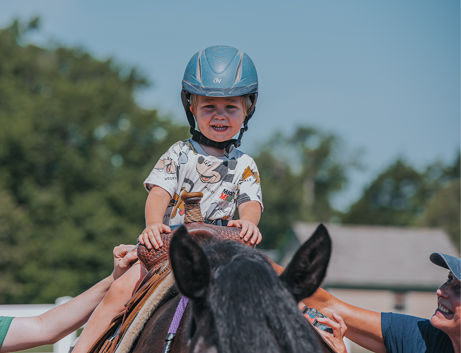 child with healmet riding horse