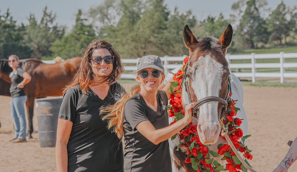 horse wearing garland and two women are standing besides