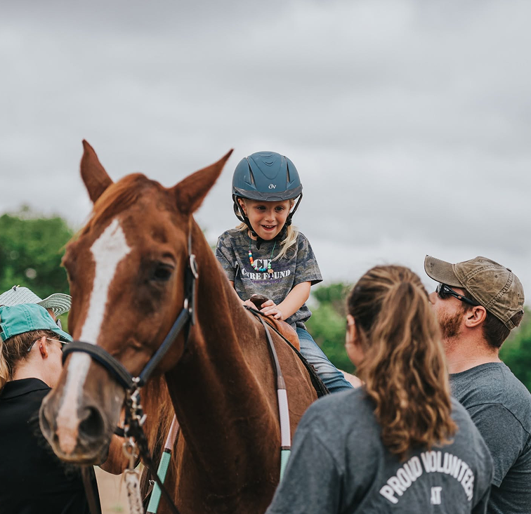 boy riding the horse with the help of volunteer